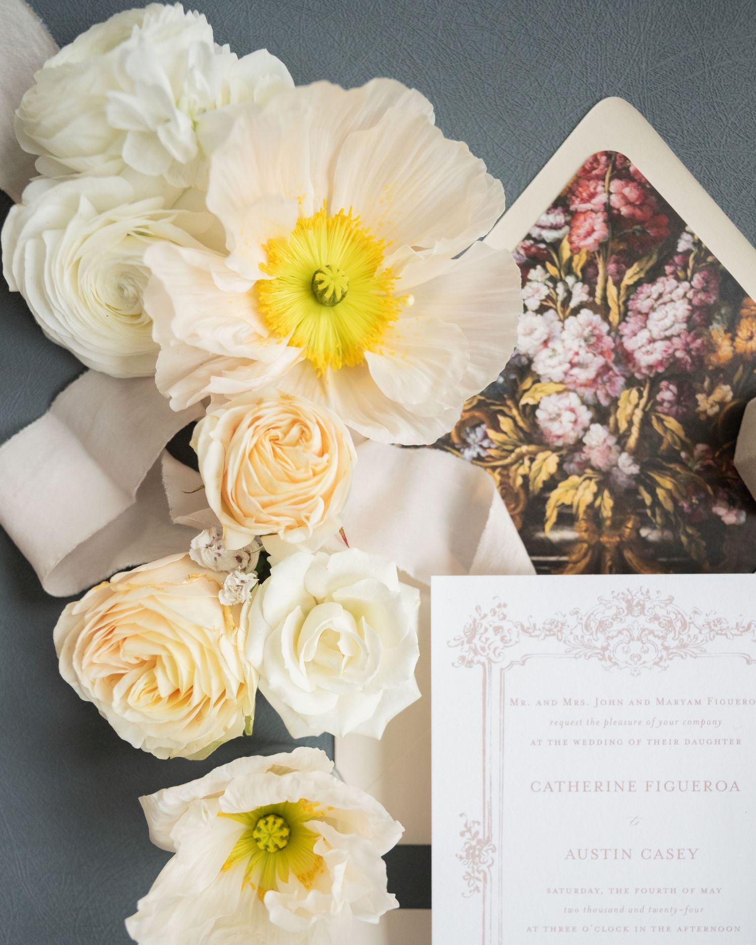 Wedding stationery flatlay with floral envelope liner and white roses against dark background.