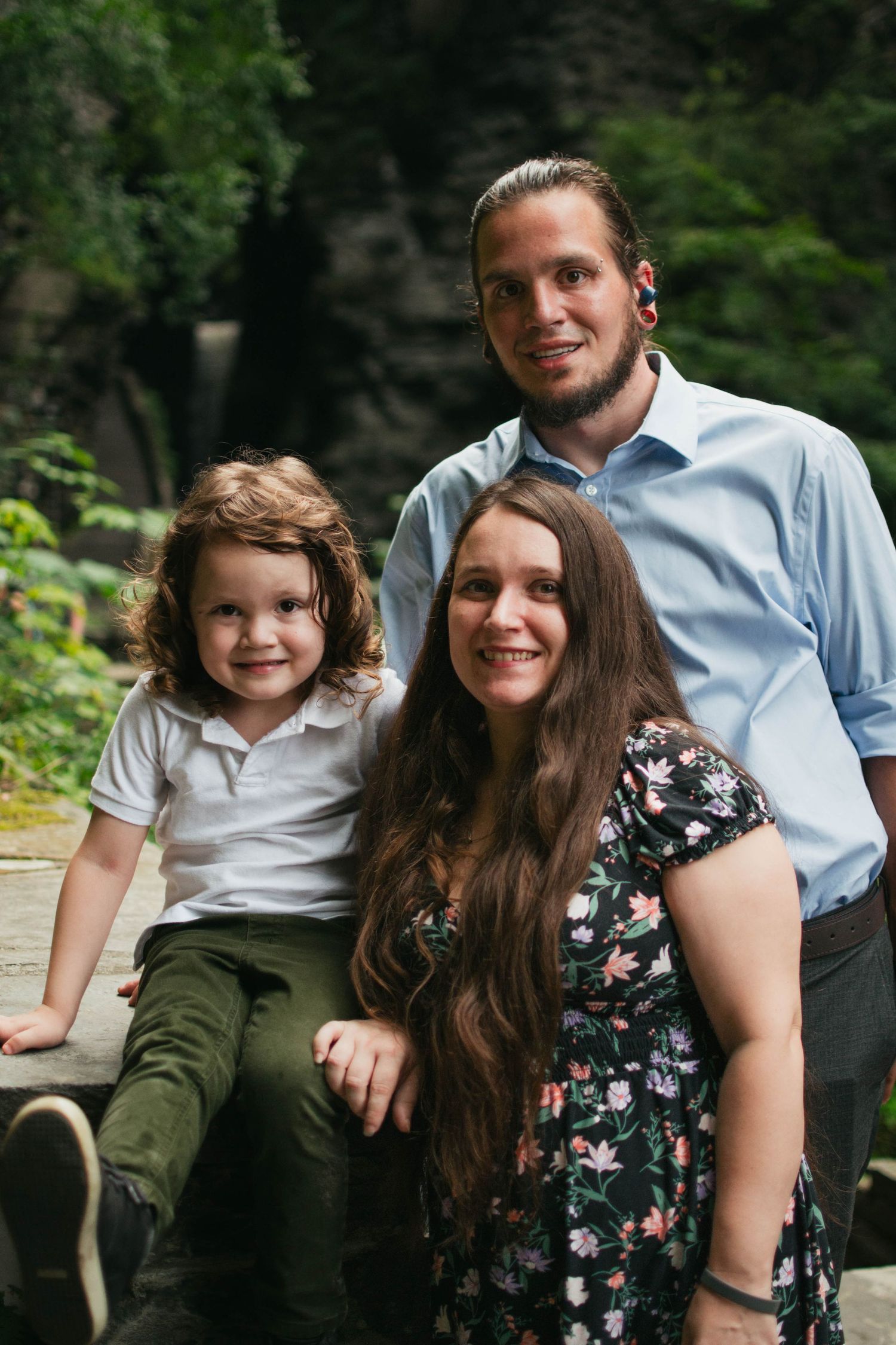A family portrait taken outdoors showing a couple and their young child in casual attire.