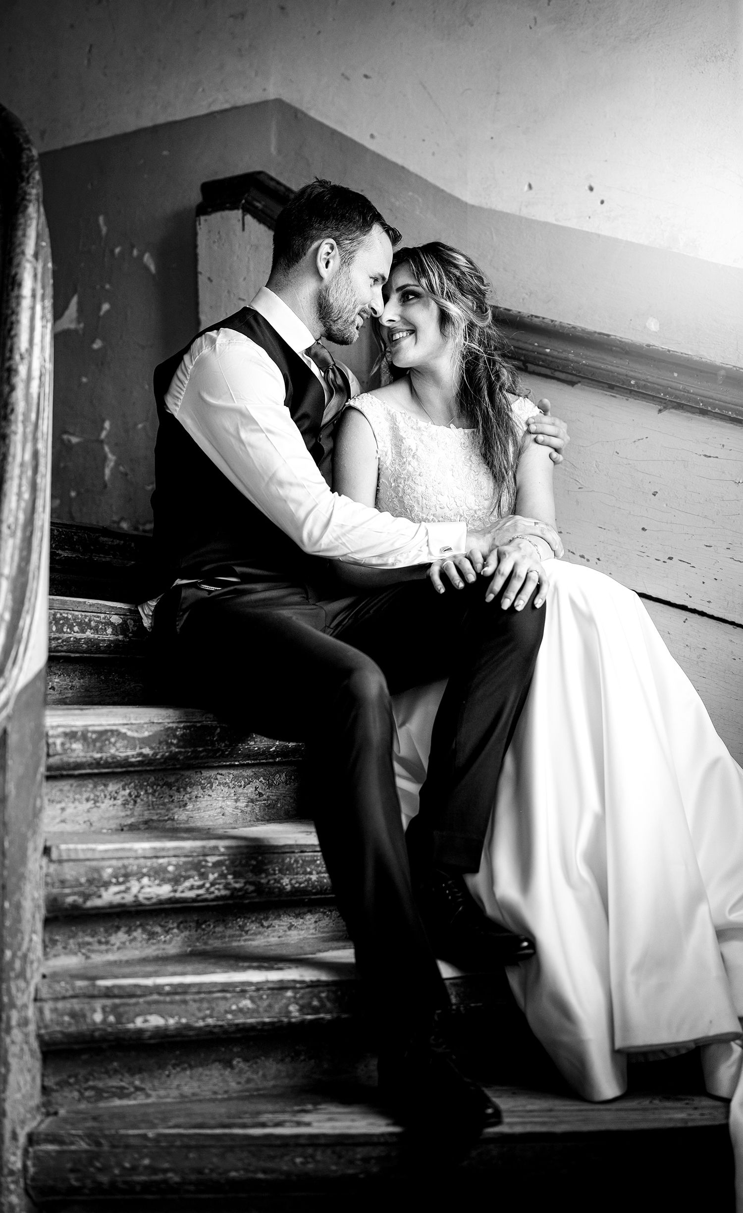 Intimate moment between couple on vintage wooden staircase in black and white.