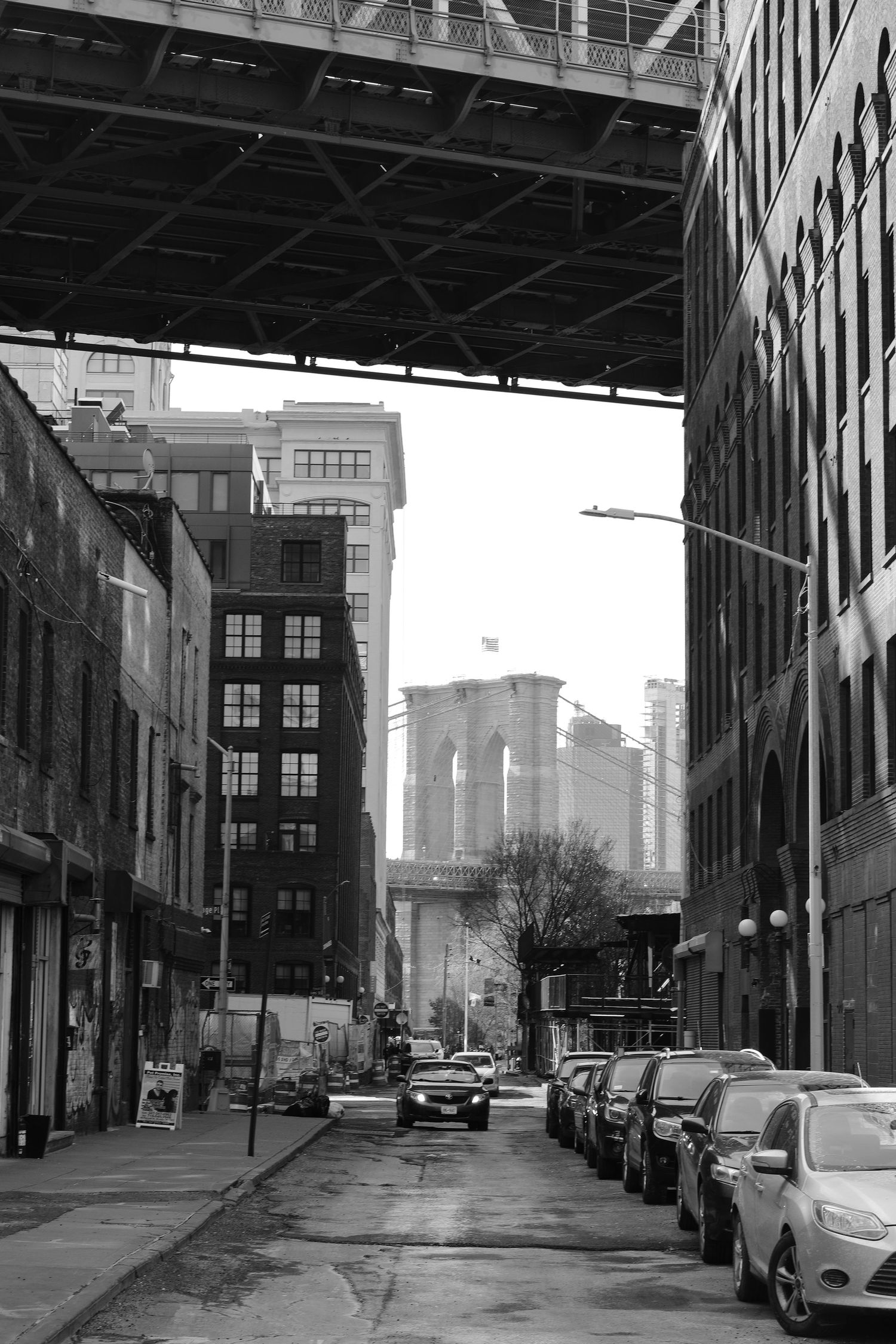 View under a bridge overpass with parked cars lining a city street.