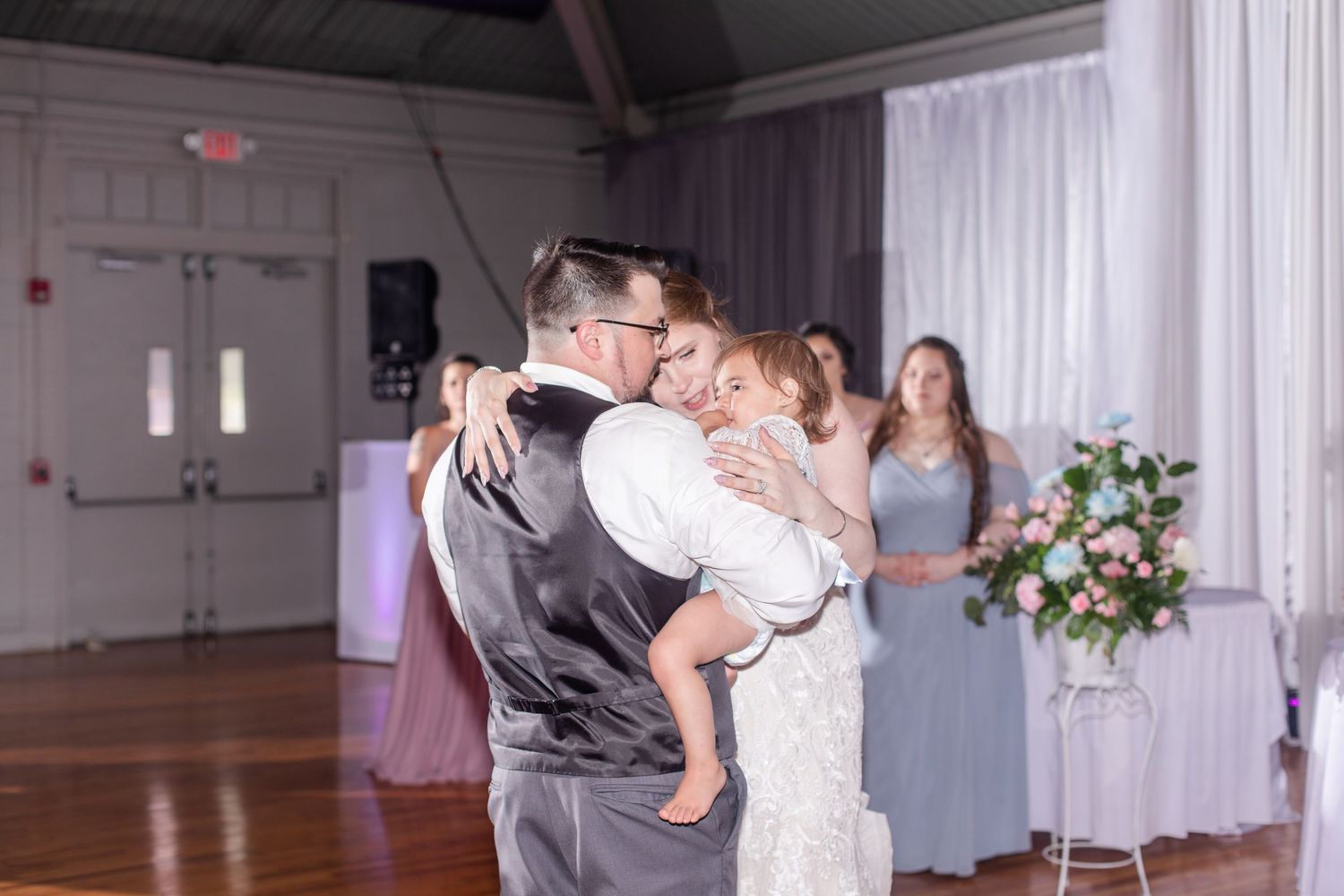 Wedding reception space featuring white drapes, hardwood floors and romantic lighting design.