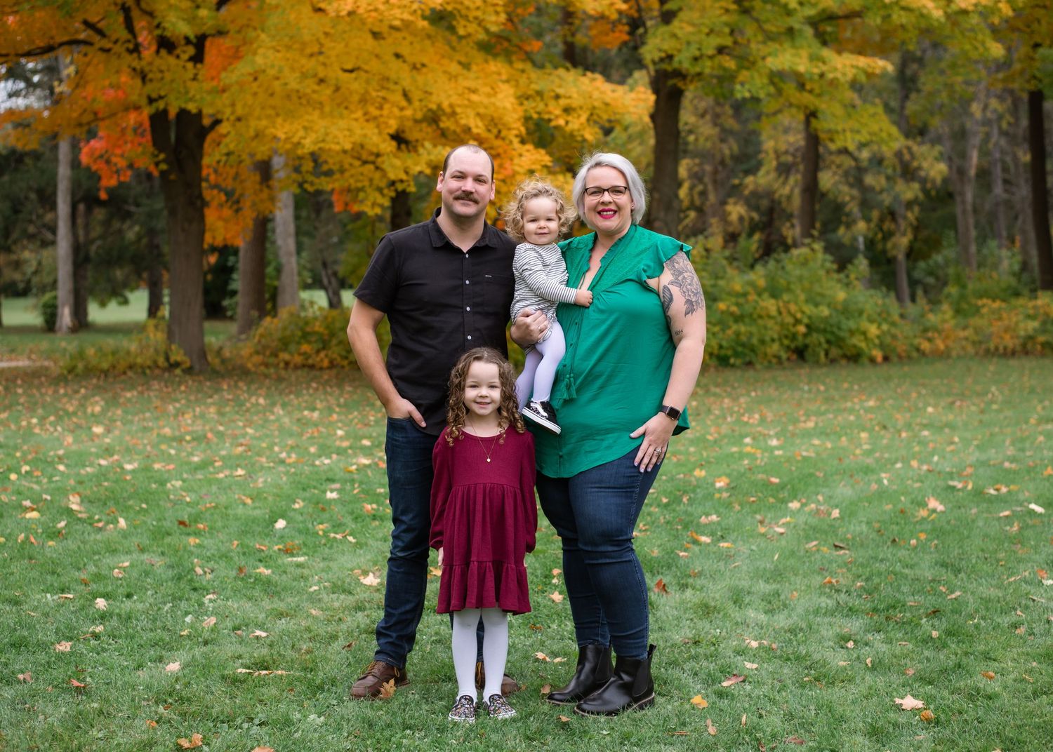 A family stands together on grass with bright autumn foliage in the background.