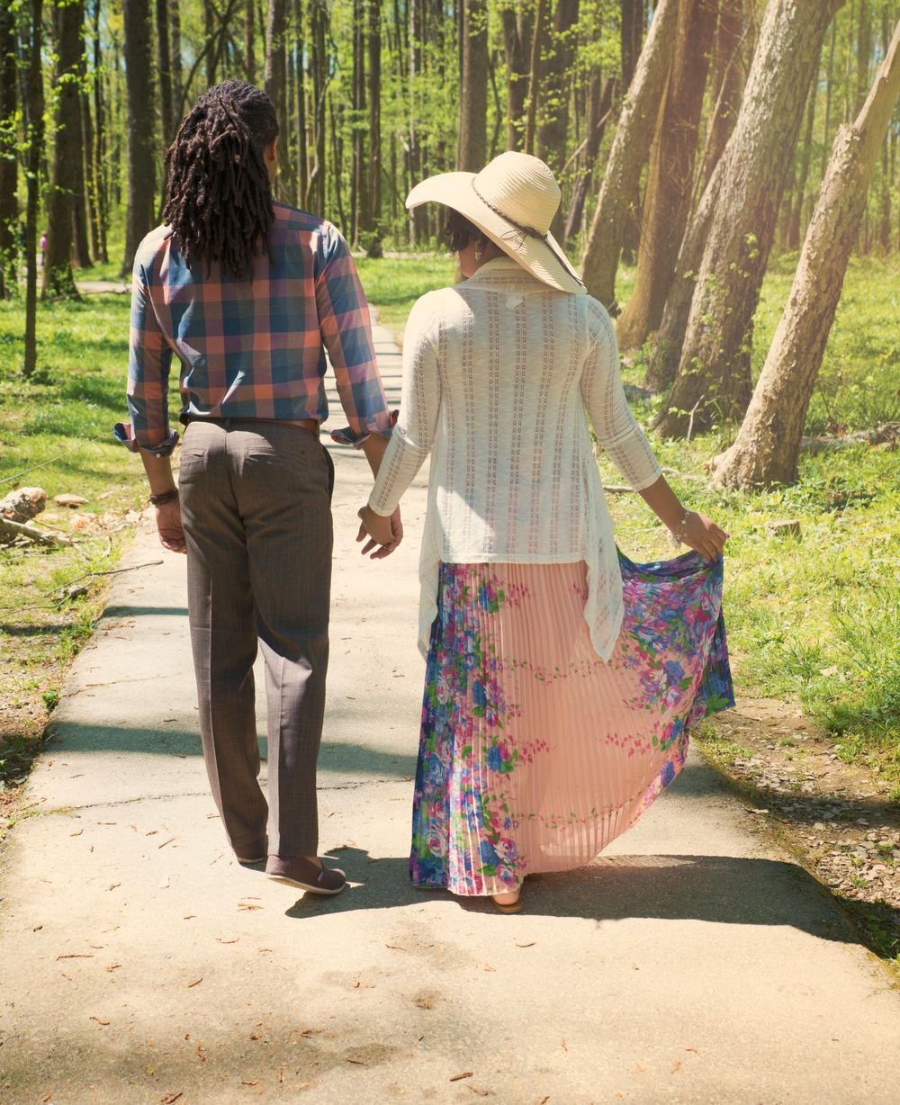 Couple walking hand in hand down a forest path on a sunny afternoon.