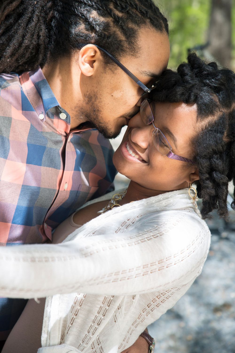 Intimate couple sharing a tender moment outdoors with sunlit trees in the background.