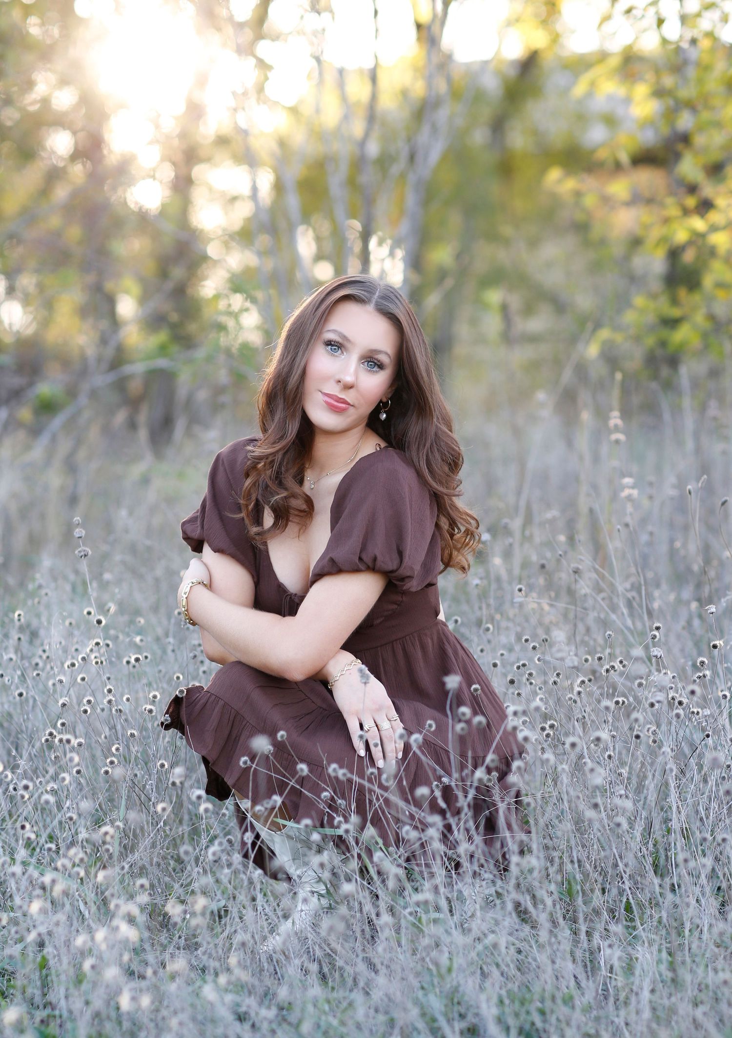 Woman in brown dress poses elegantly in field of dried wildflowers during golden hour.