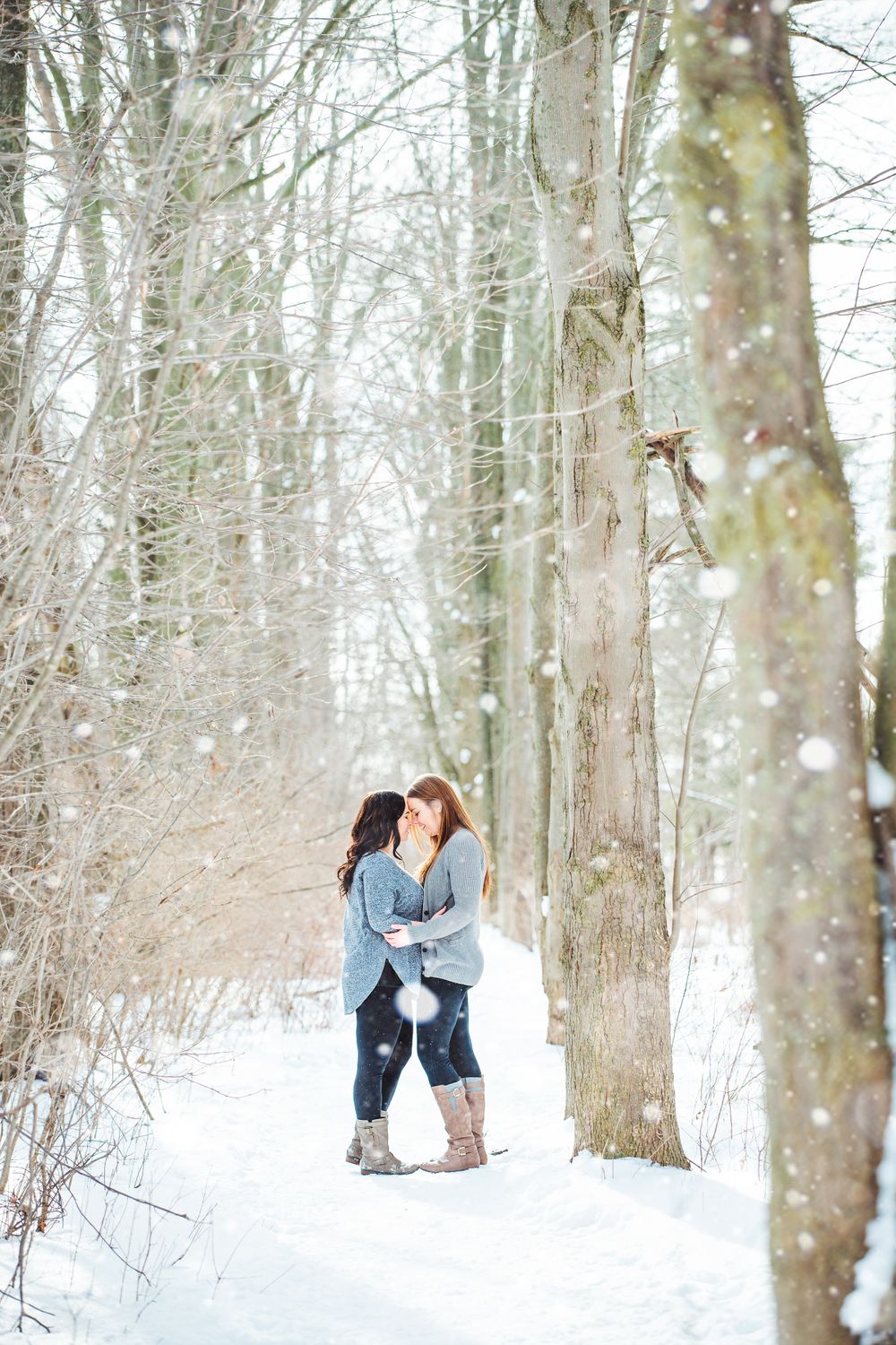 Winter engagement photos in snowy forest with bare trees creating magical atmosphere.