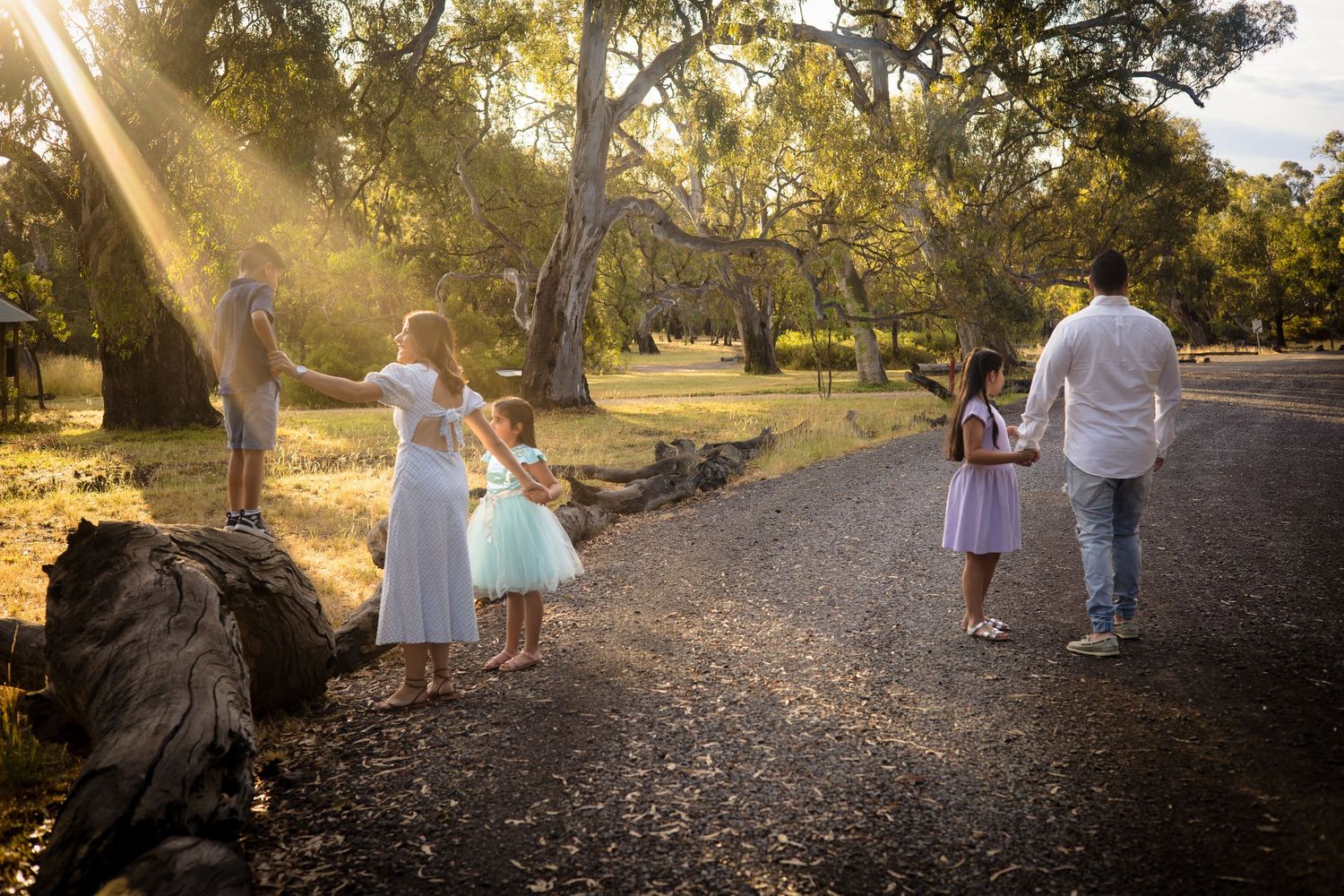 Family walking together on a gravel path during golden hour in a rustic outdoor setting.
