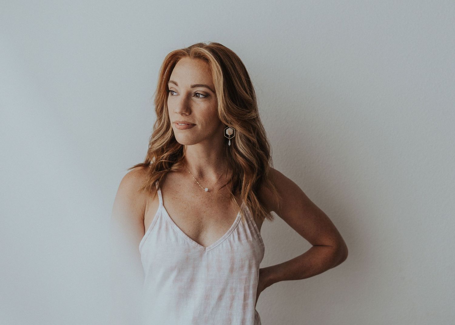 A redhead woman stands against a white wall