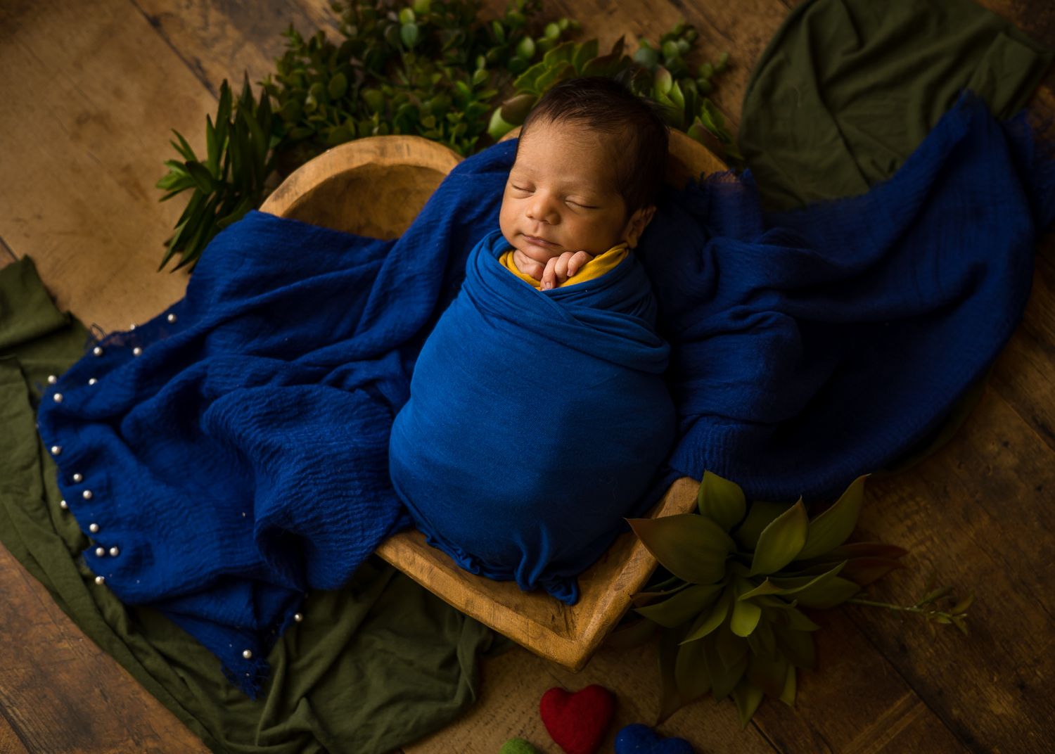 Sleeping newborn wrapped in deep blue blanket on wooden basket prop.
