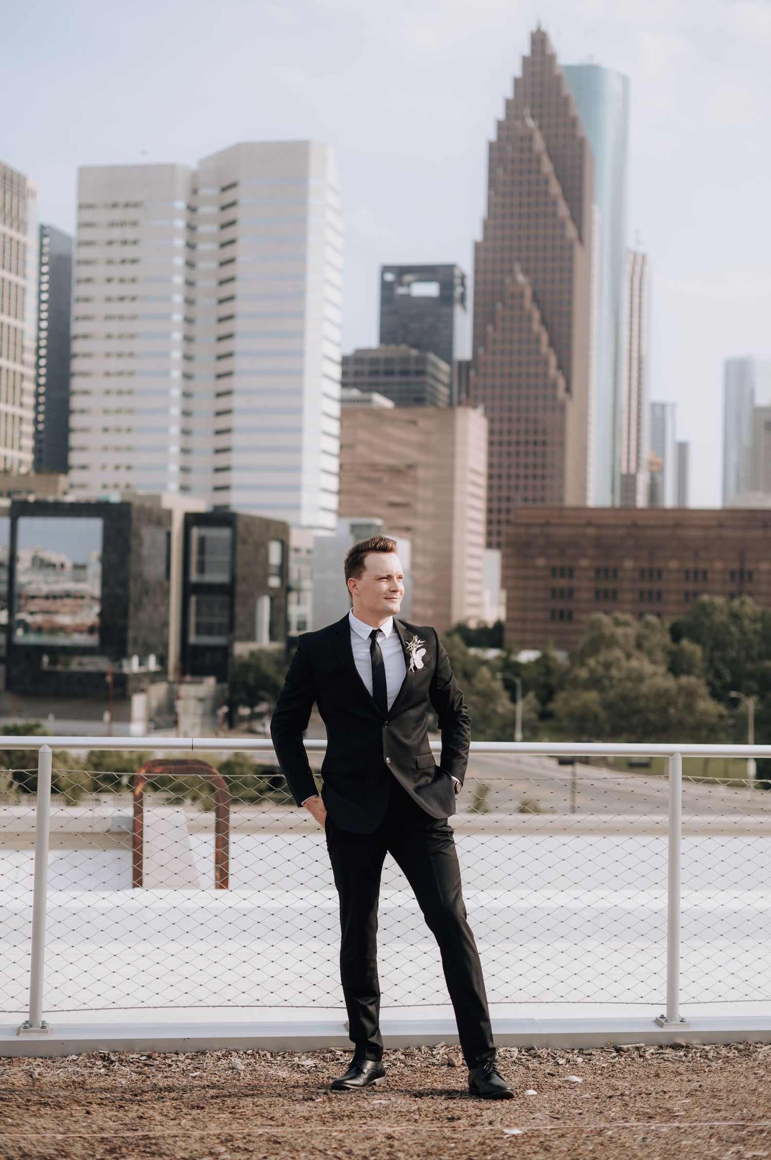 Groom poses confidently in black suit with Houston skyline in background.