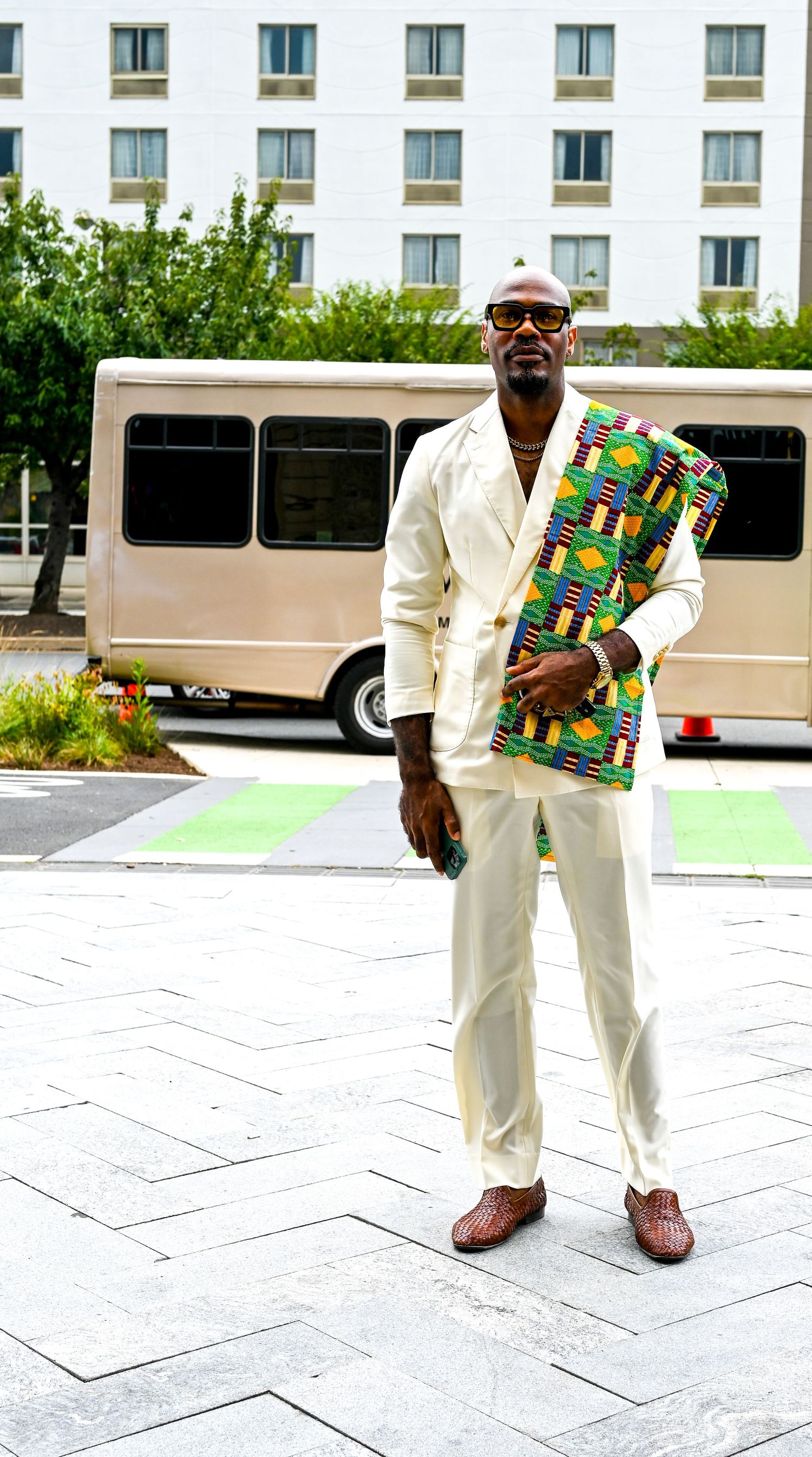 All-white outfit with colorful African print clutch photographed against white building exterior.