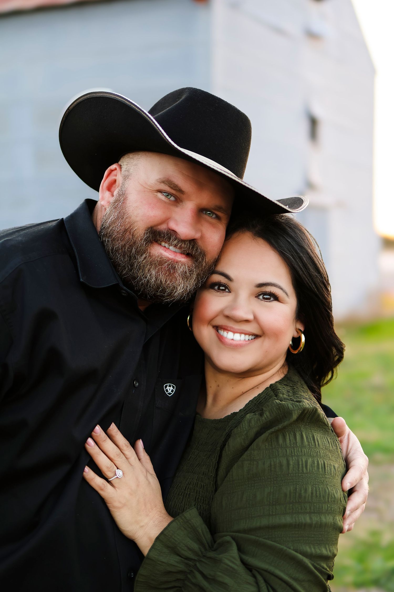 Couple in casual attire posing together outdoors, one wearing a western hat.