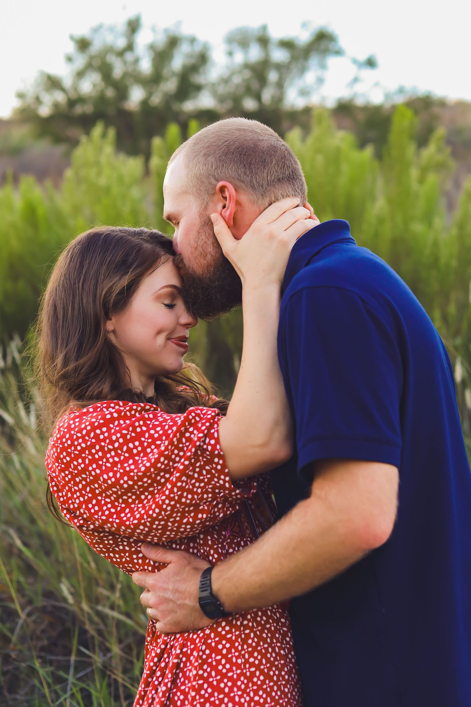 Intimate couple portrait in natural setting with woman in red dress touching man's face.