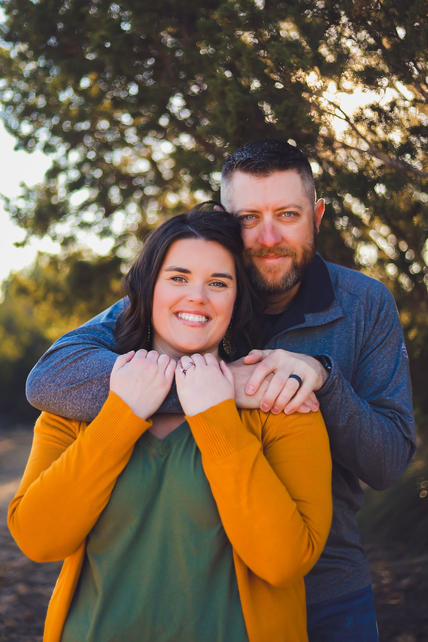 A couple embraces outdoors, with one wearing a bright orange sweater and the other in navy blue.