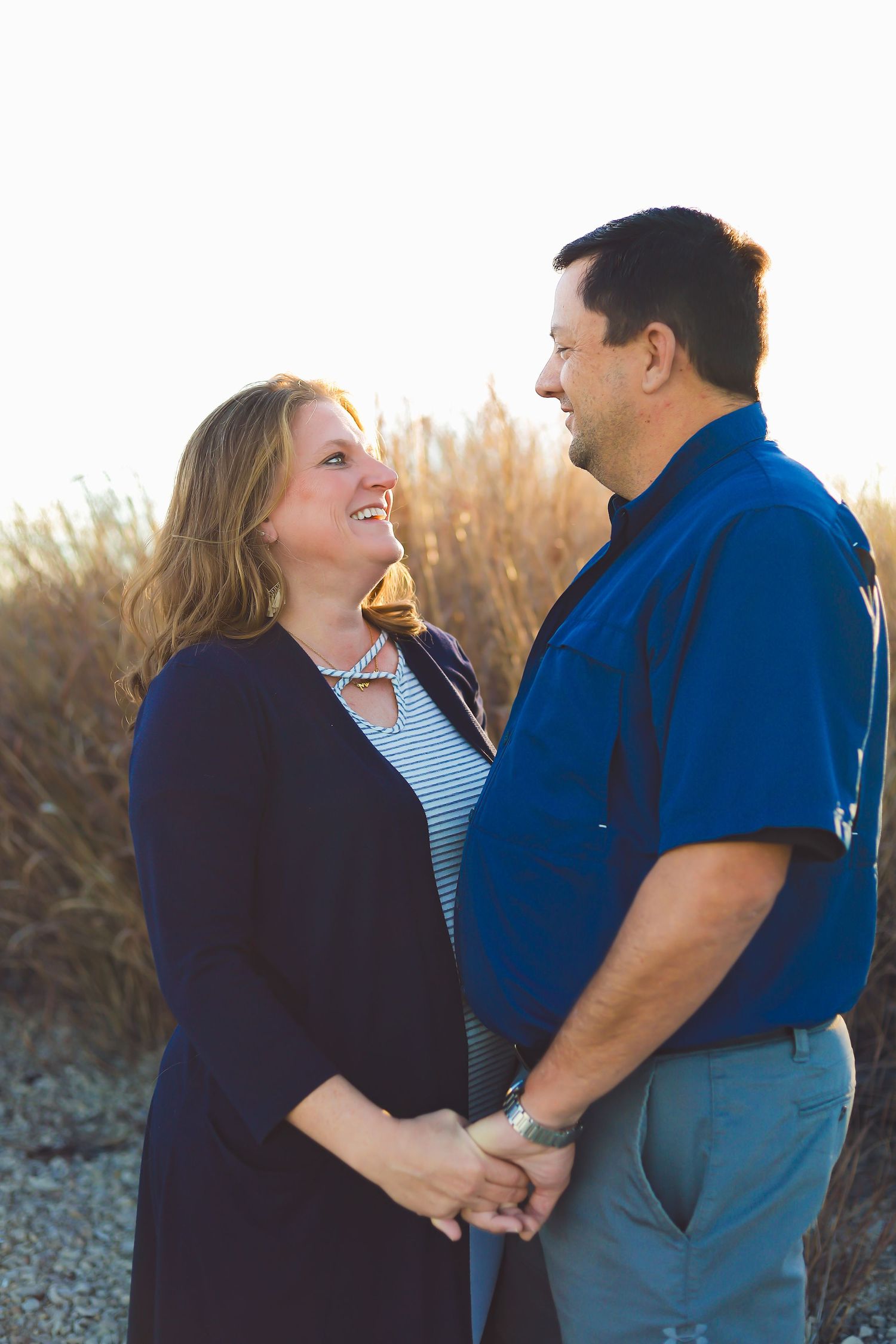 A couple shares a loving moment while holding hands in front of tall grass at sunset.