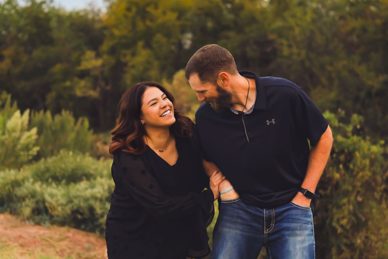 A couple laughs together outdoors while sharing a candid moment at sunset.