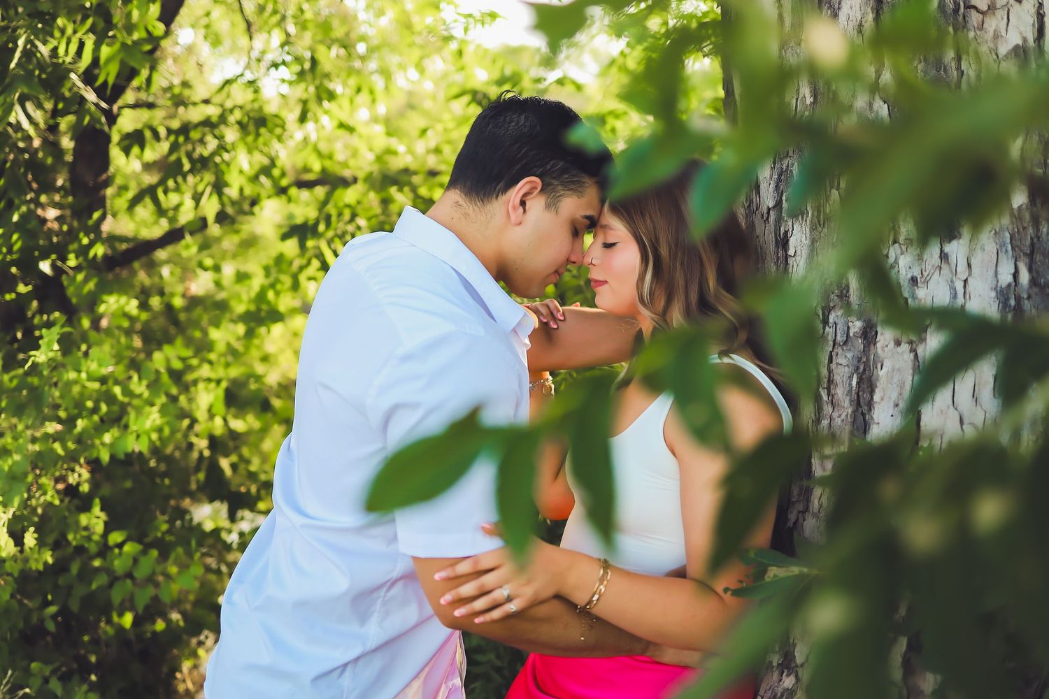 A romantic couple shares an intimate moment among green leaves and sunlight.