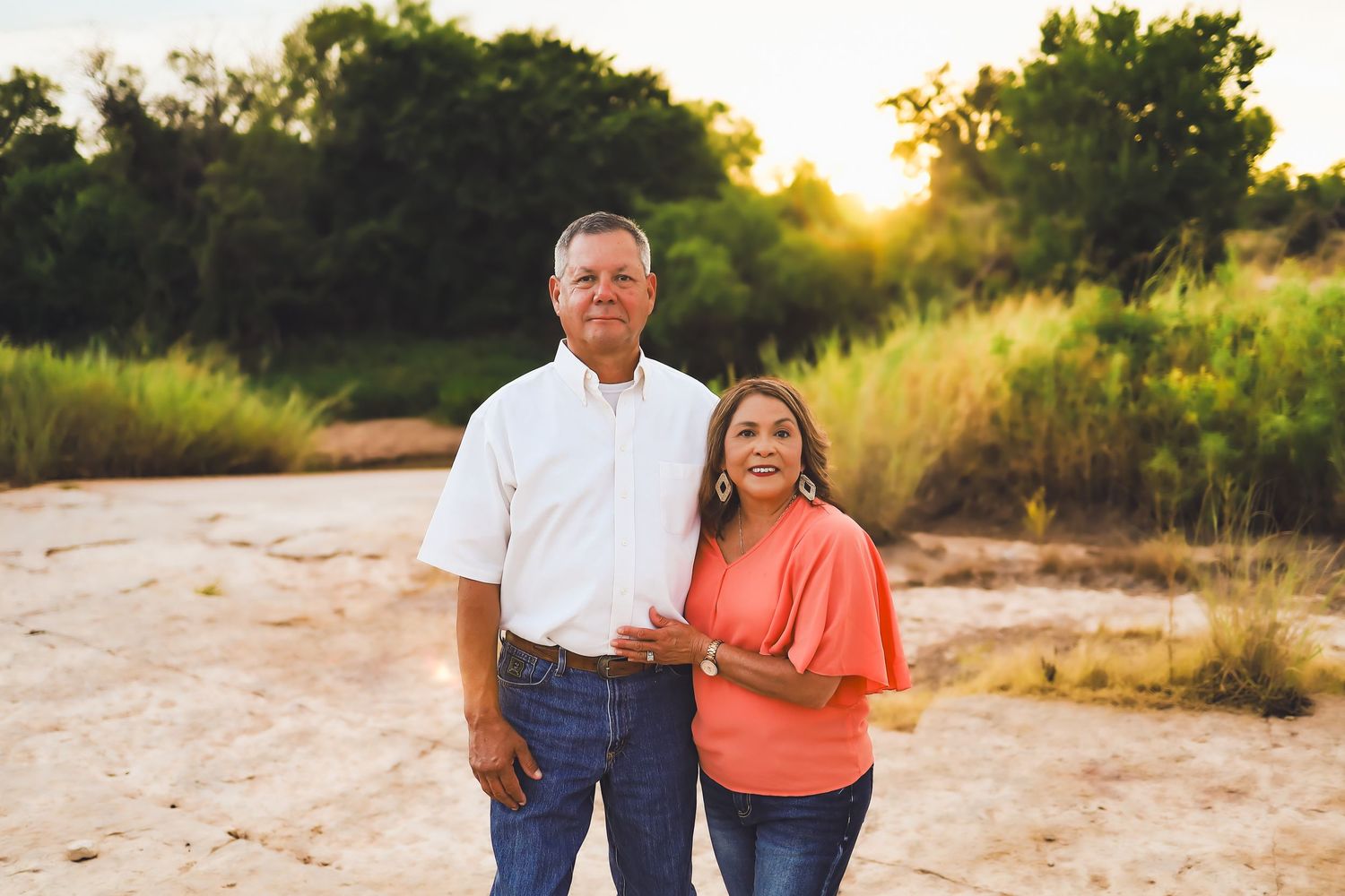 A couple stands together on a dirt path during golden hour with tall grass in the background.