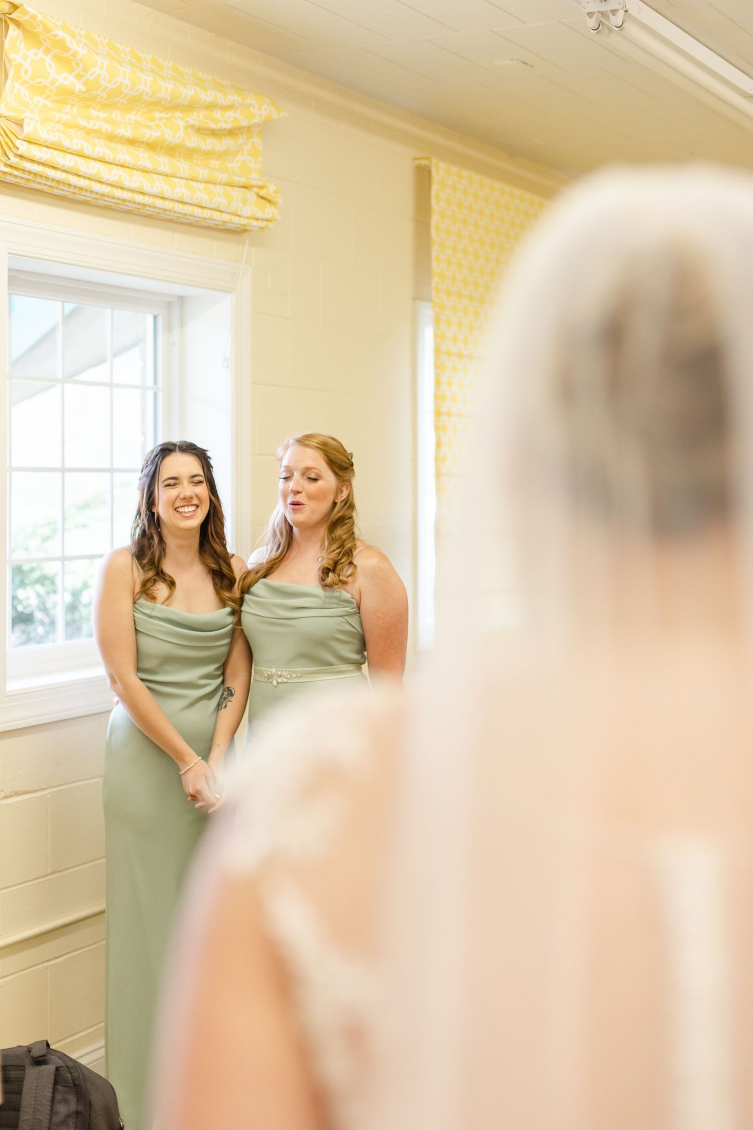 Bridesmaids in sage green dresses share a candid moment during wedding preparations.