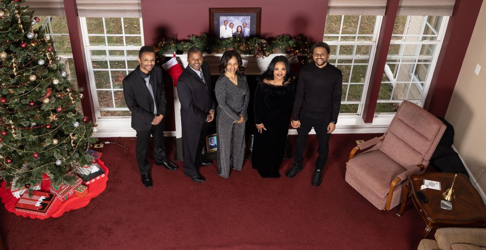 Group holiday photo with decorated Christmas tree and living room setting.