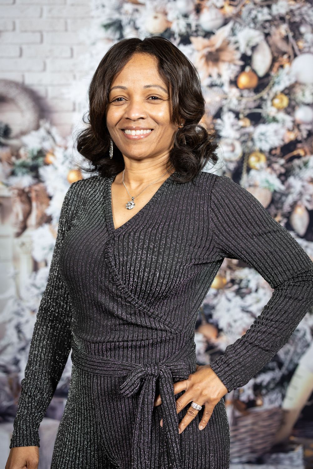Woman in gray knit wrap dress poses against holiday backdrop with decorated tree.