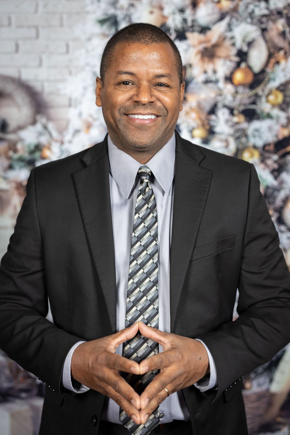 Professional portrait of person in business suit with striped tie against holiday backdrop.