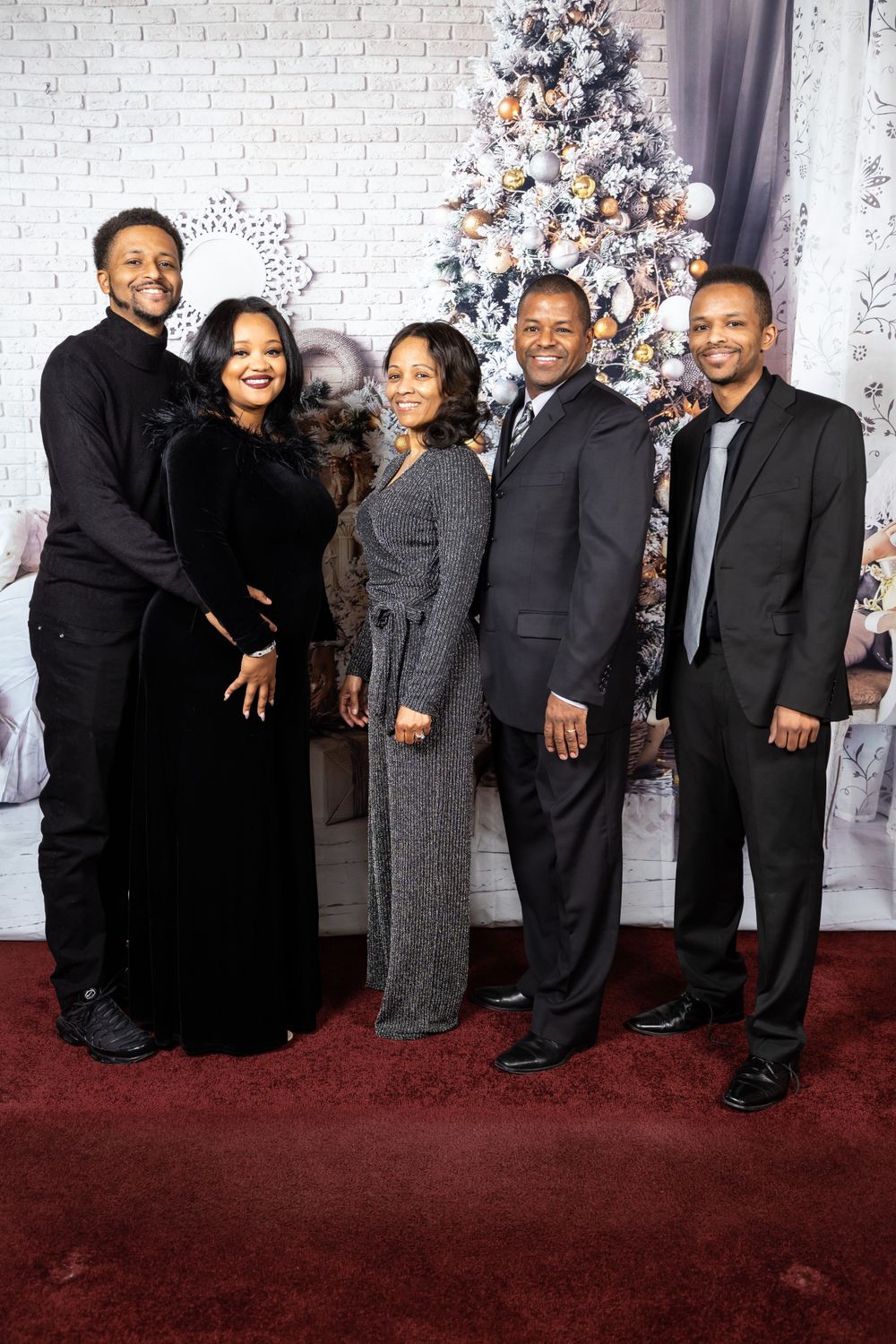 Group portrait of five people dressed formally in front of a white Christmas tree and brick wall backdrop.
