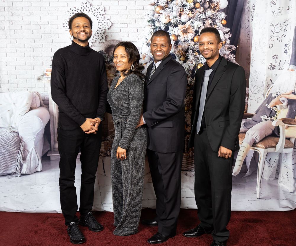 Four people in formal dress stand together in front of a decorated Christmas tree and white backdrop.