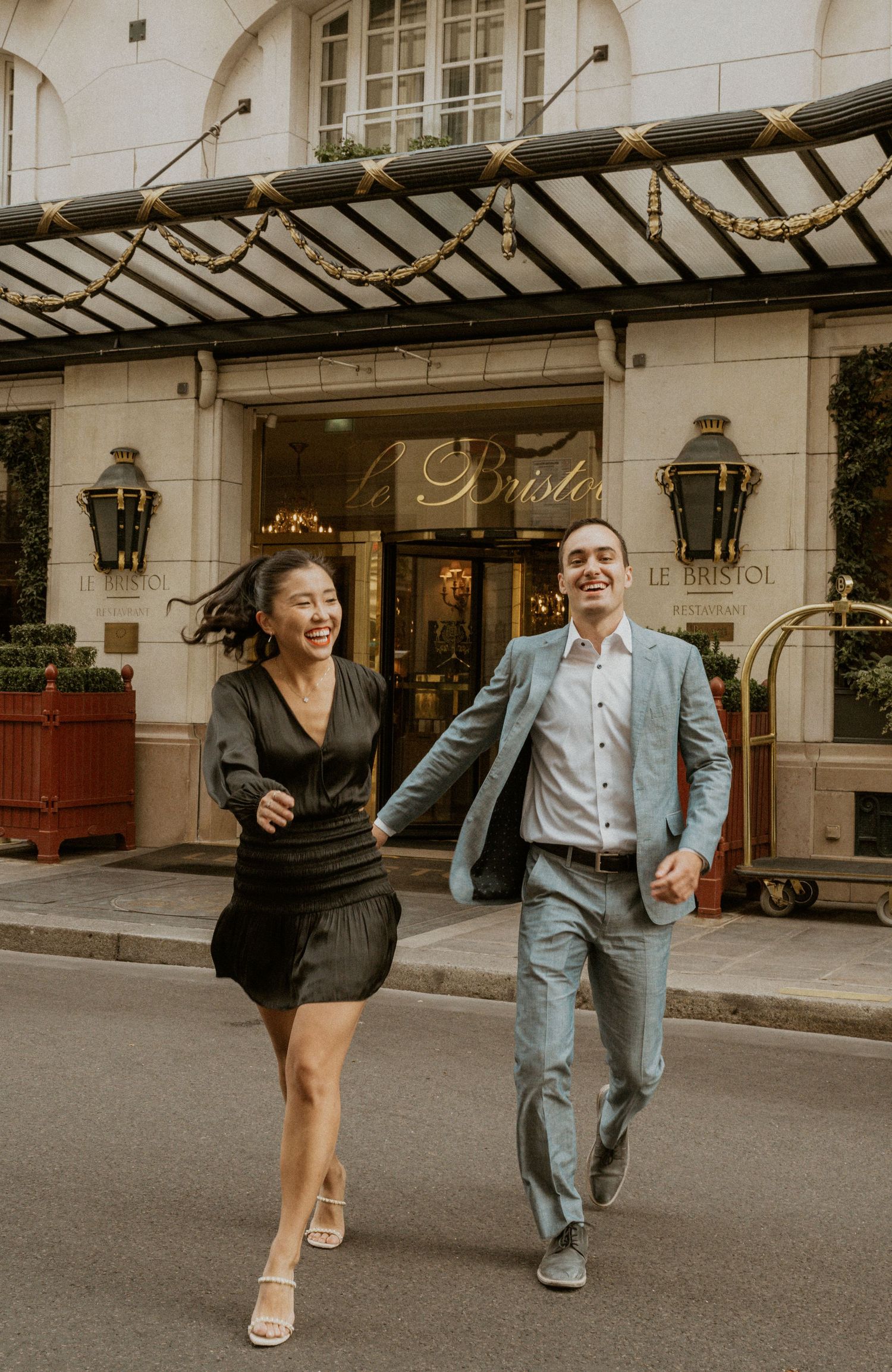 A couple laughs together while walking outside a luxurious hotel entrance.