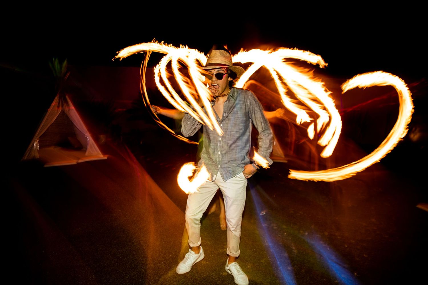 Man in hat poses dramatically with fire spinning light trails against dark night sky.