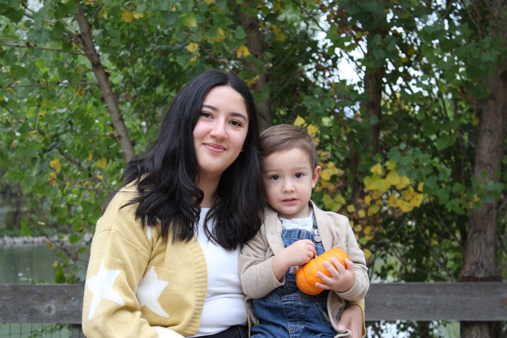 A pair sharing a tender moment while holding a small orange pumpkin in an autumn garden setting.