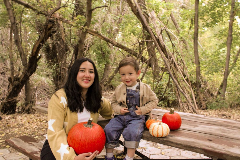 Two people sitting with pumpkins on wooden surface in autumn forest setting.