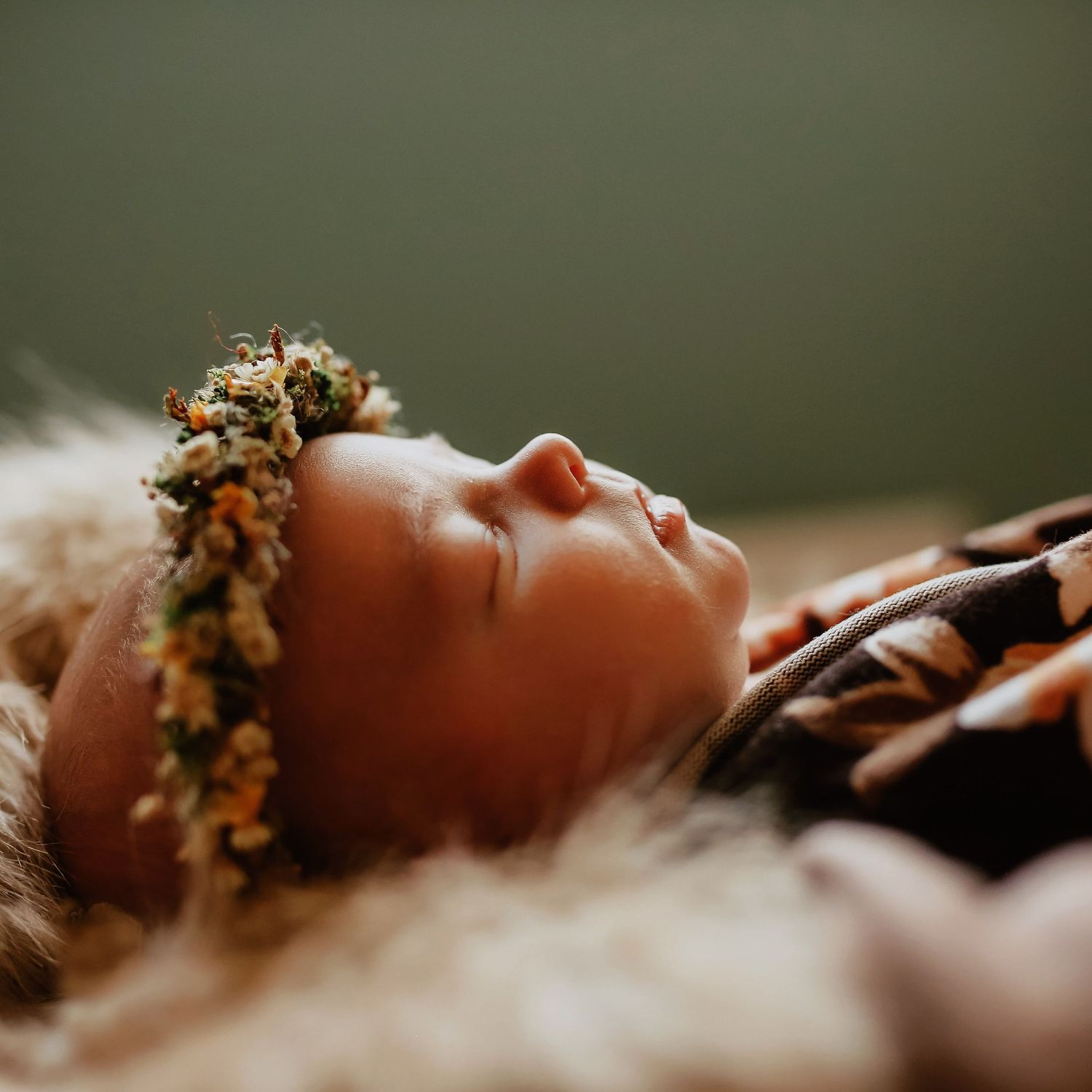 A delicate floral crown adorns a figure lying peacefully against a soft, blurred green background.