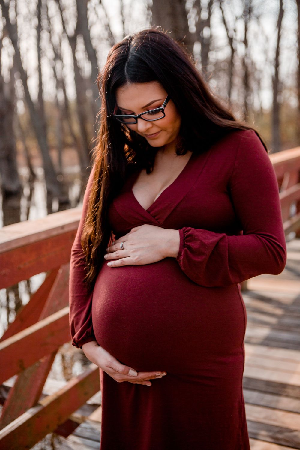 A maternity portrait on a wooden bridge showcasing an expectant mother in a burgundy dress.