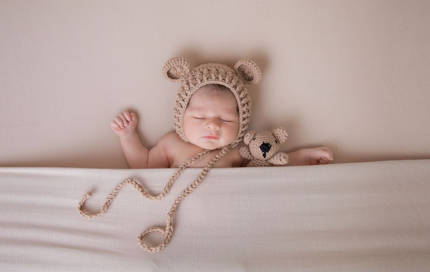 Newborn shoot, baby wearing knitted teddy ears hat, cuddling matching knitted teddy, beige stretch backdrop