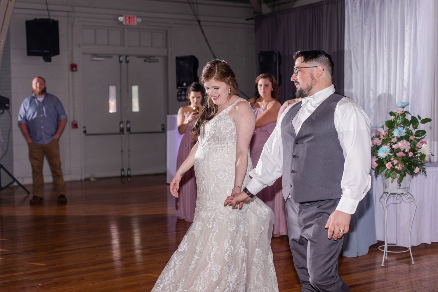 Wedding reception dance floor with white draping and floral arrangements in an industrial-style venue.