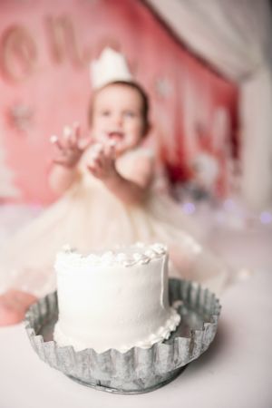 Artistic blurred cake smash photo with white cake on silver platter against pink background.