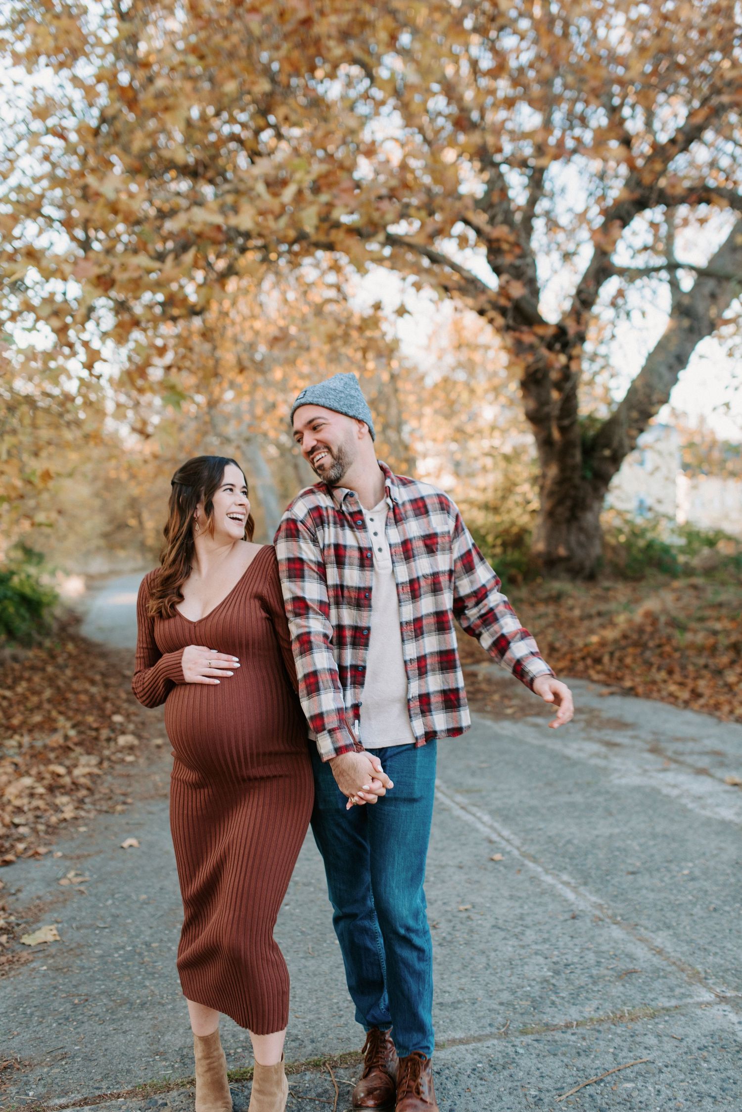 Playful autumn couples photoshoot with brown sweater and plaid shirt among fallen leaves.