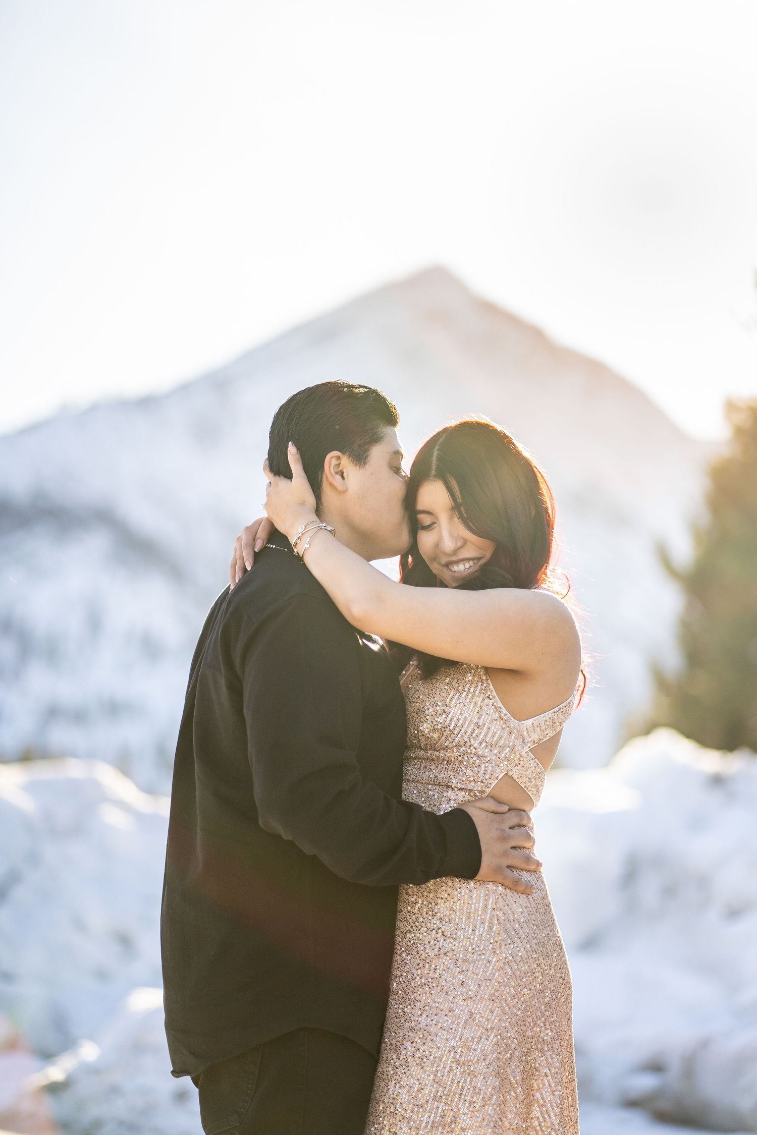 A couple embracing in formal wear against a snowy mountain backdrop at golden hour.