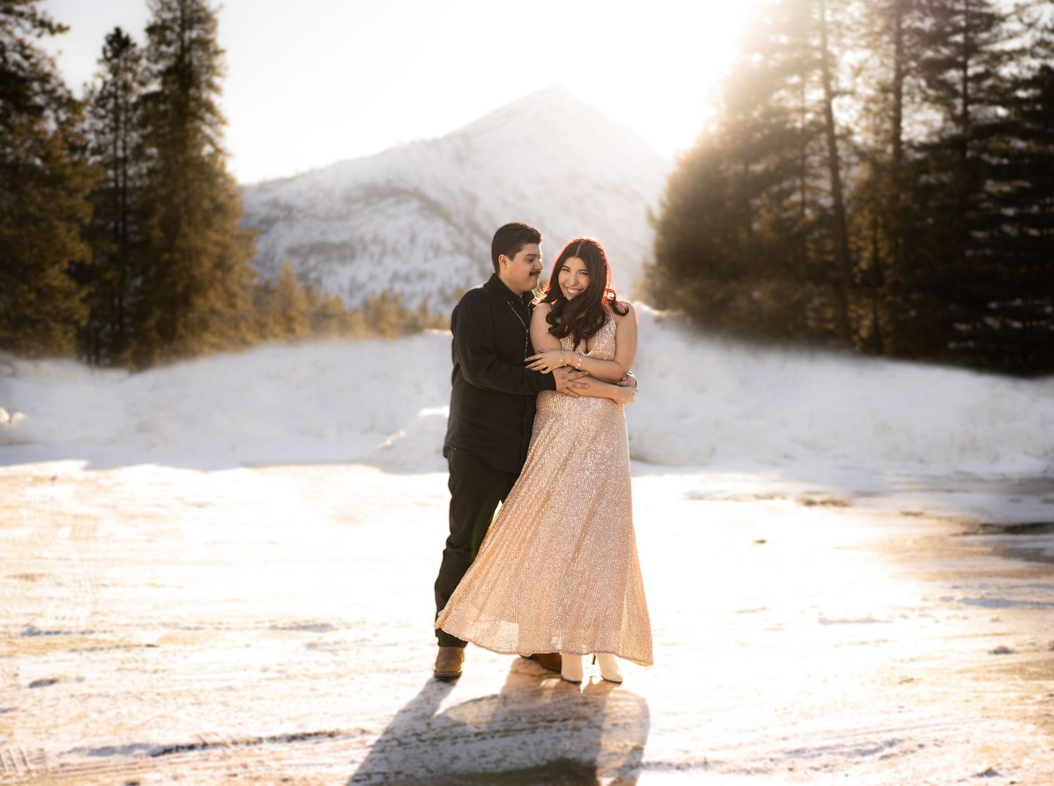 A romantic couple dancing together in a snowy mountain landscape at sunset.