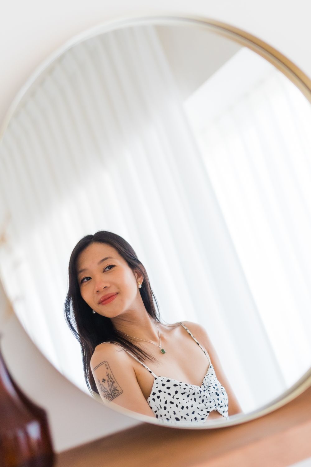 A mirror selfie shows a person in a white spotted dress with visible tattoos.
