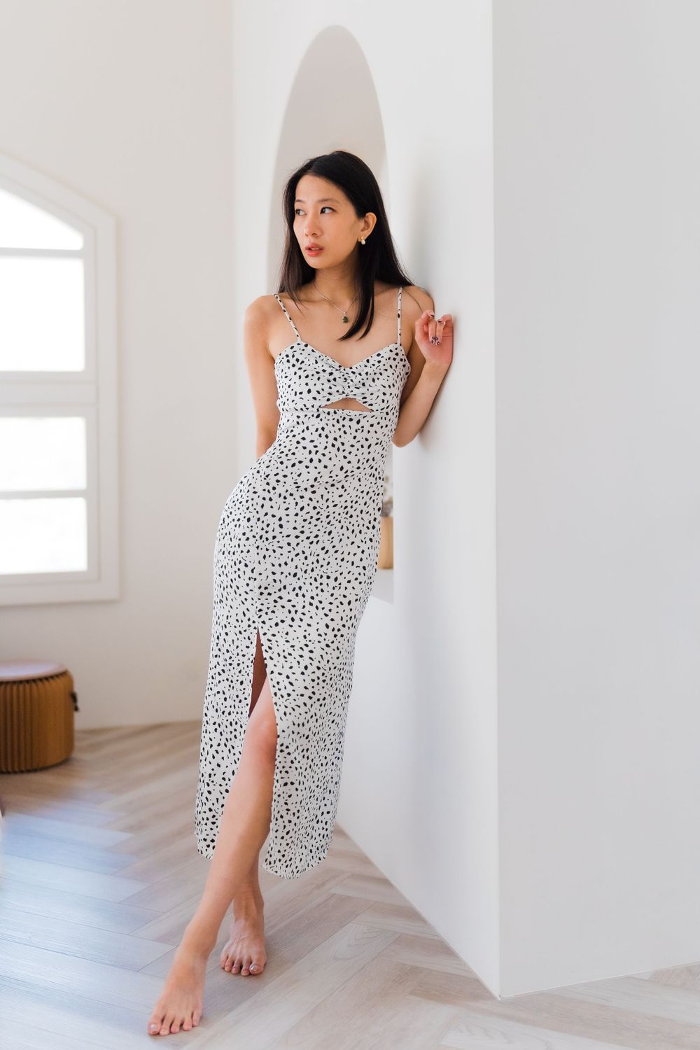 A person wearing a spotted dress with a side slit poses elegantly against an arched wall.