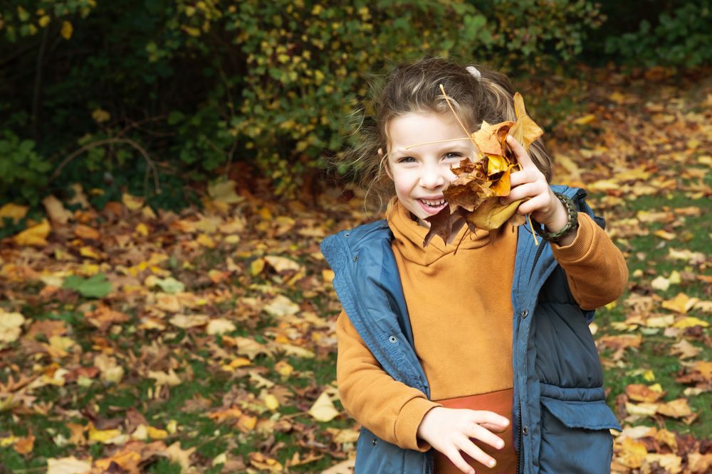 Lachend meisje speelt met een herfstblad in het bos – spontane kinderfotografie Arnhem