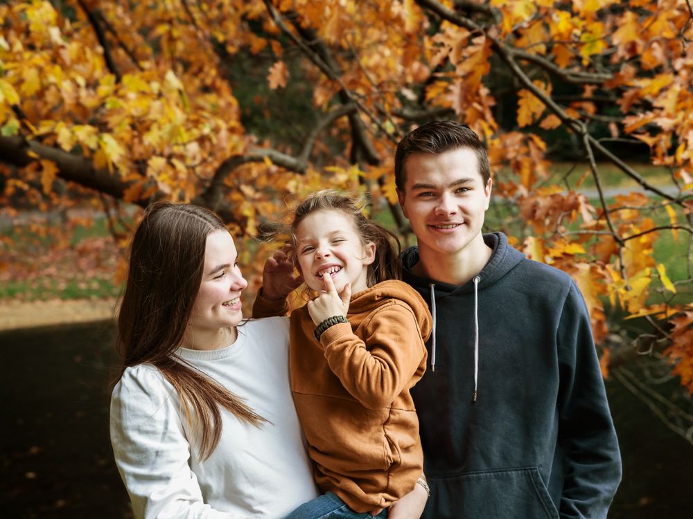 Warm familieportret van ouders met kind tussen de herfstbladeren – familiefotografie Arnhem