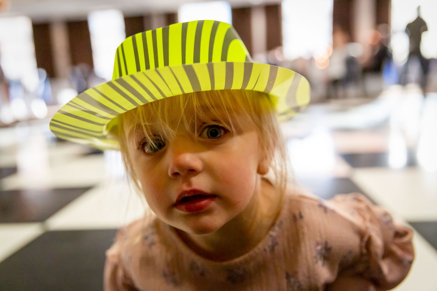Little girl wearing a plastic hat leans right into the camera during the wedding reception at the Crowne Plaza Hotel