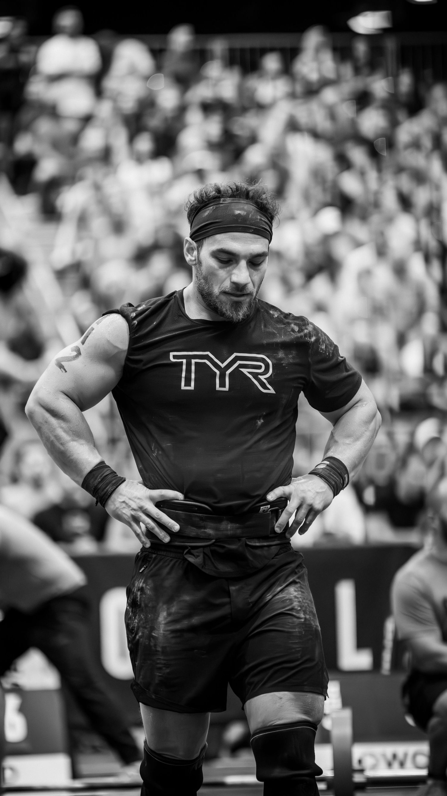 Athletic competitor wearing TYR shirt at sporting event with crowd in background.
