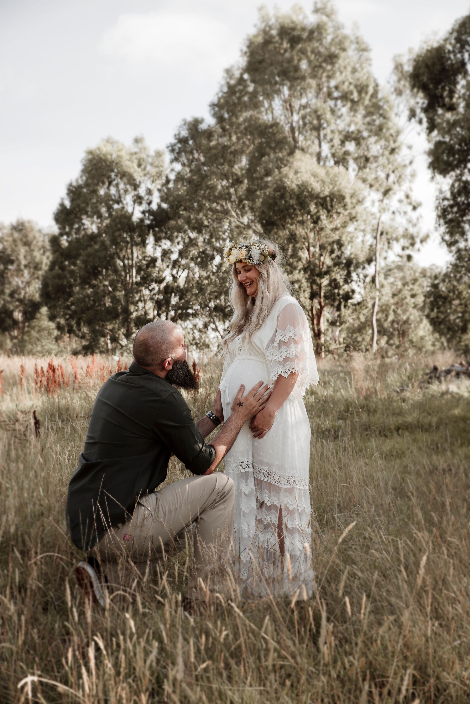 A couple shares an intimate moment in a field surrounded by tall eucalyptus trees at sunset.