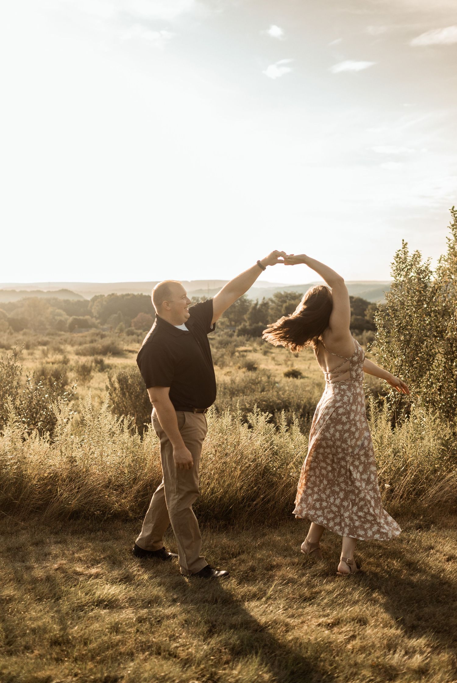 A couple dancing together on a hilltop during sunset in a romantic setting.