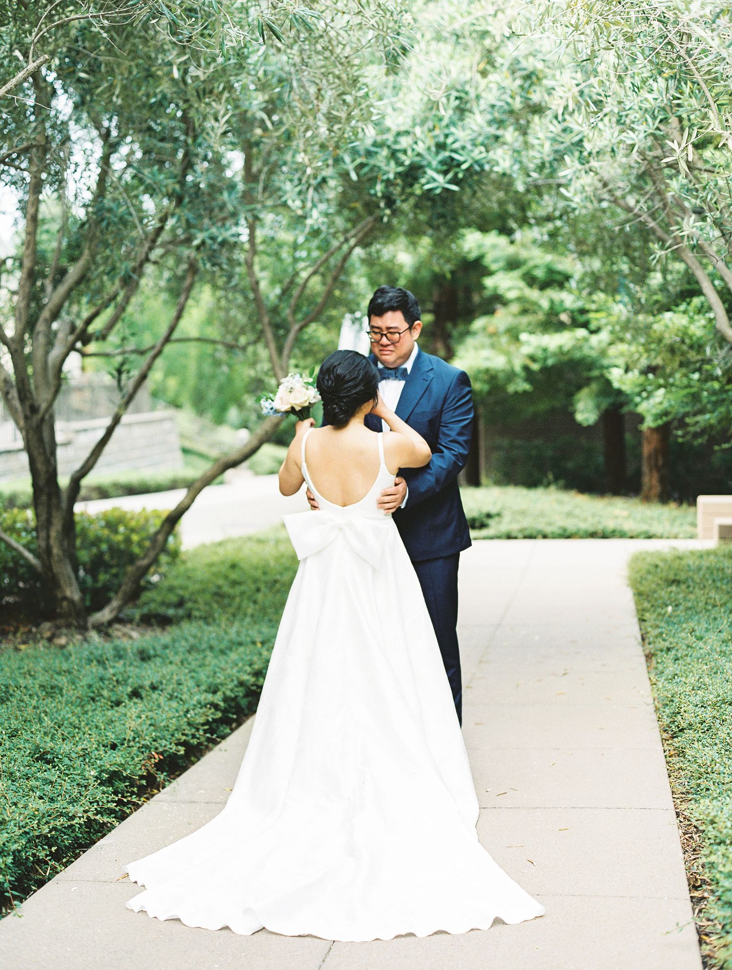 Wedding couple sharing private moment on garden pathway surrounded by trees.