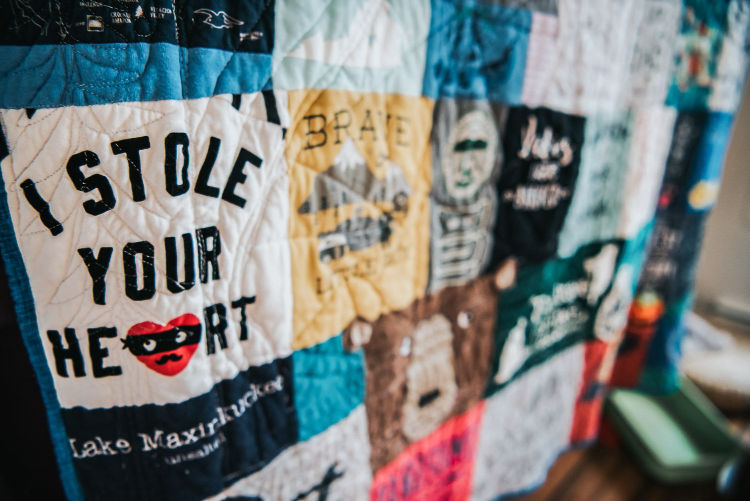 Memory quilt made with a patchwork of baby clothes is held up and a piece says 'I Stole Your Heart'